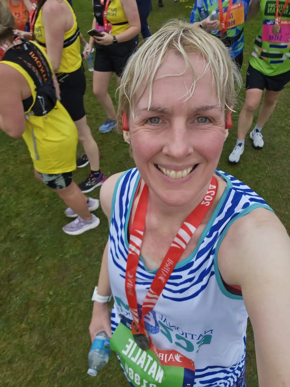 A white women, with visible eczema on her face, is wearing a National Eczema Society running vest. There is a Great North Run 2024 finisher medals around her neck.