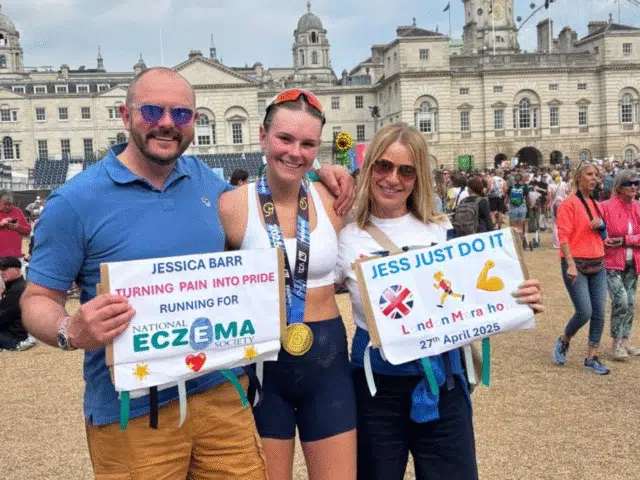 A group of three people. The woman in the middle is wearing running clothing with a London Marathon finishers medal around her neck. The people either side are holding supportive posters for the runner in the middle.