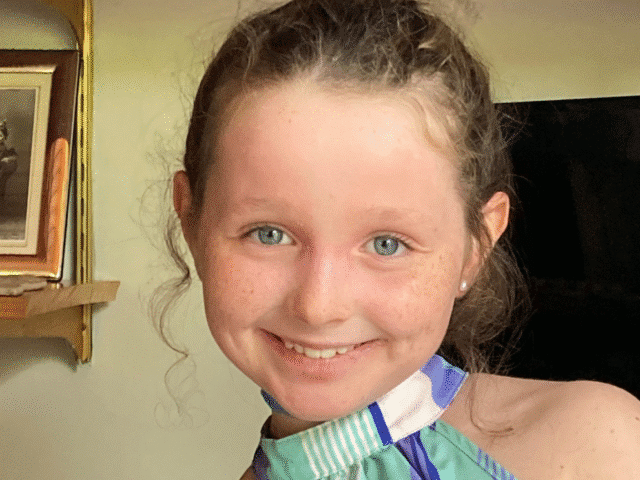 Close-up of a smiling young girl with curly hair, wearing a striped top.