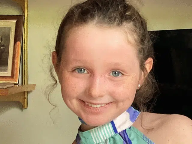 Close-up of a smiling young girl with curly hair, wearing a striped top.