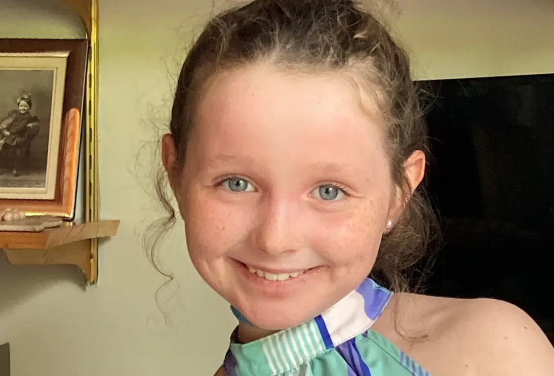 Close-up of a smiling young girl with curly hair, wearing a striped top.