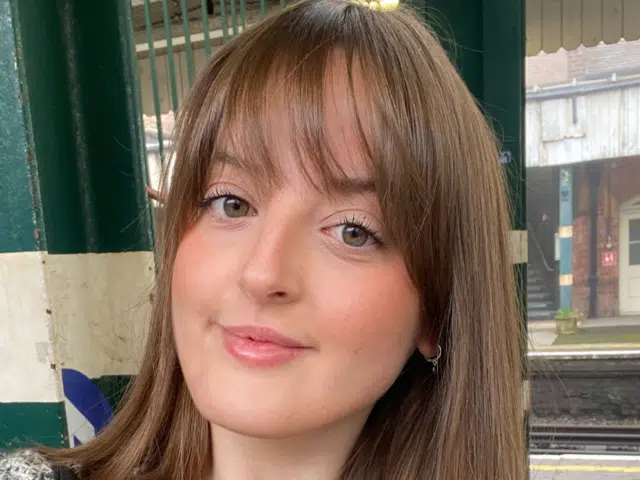 A young white women with long brown hair and a fringe looking ahead.